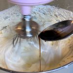 spoon adding vanilla to frosting batter